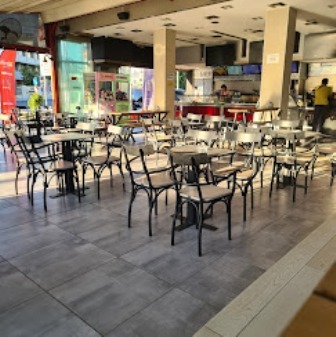 Empty indoor cafe seating area in a shopping mall, metal chairs and small tables arranged in rows with storefronts in the background.