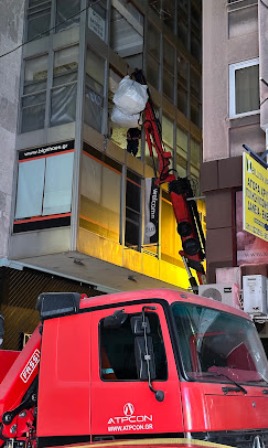 Red crane truck in a city street lifting a large white bag toward a tall, windowed building edge.