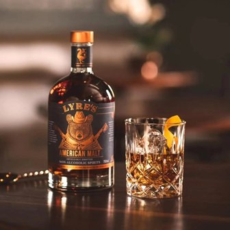 Bottle of Lyre's American Malt non-alcoholic spirits next to a tumbler filled with ice and a lemon twist on a bar.
