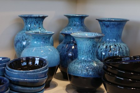 Collection of blue glazed ceramic vases and bowls arranged on a shelf.