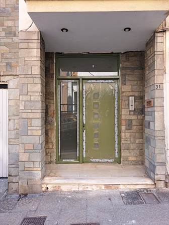 Green front door with glass panel beside a stone brick entrance, building number 31 visible.