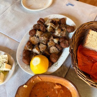 Plate of crispy cubed potatoes with a lemon wedge on a dining table, near a bread basket and a bowl of tomato sauce.