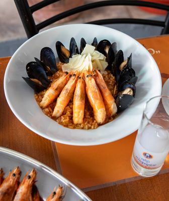 Bowl of paella with shrimp arranged around the rim, mussels along the inner edge, and a dollop of butter on top.