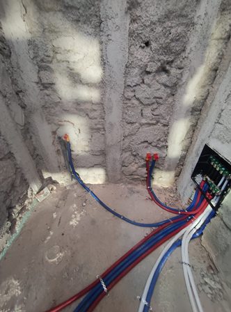 Exposed electrical cables inside a wall under construction, blue and red wires connected to a small terminal and a black junction box to the right.