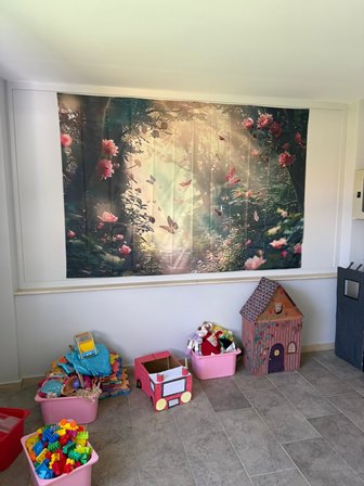 Playroom with a wall-size forest mural and colorful toy bins, including a pink dollhouse on a tiled floor.
