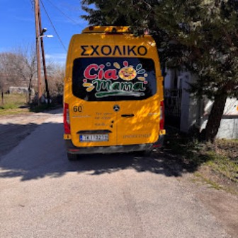Rear view of a yellow school bus parked on a sunny street, featuring a Greek 'ΣΧΟΛΙΚΟ' sign and a colorful back logo.