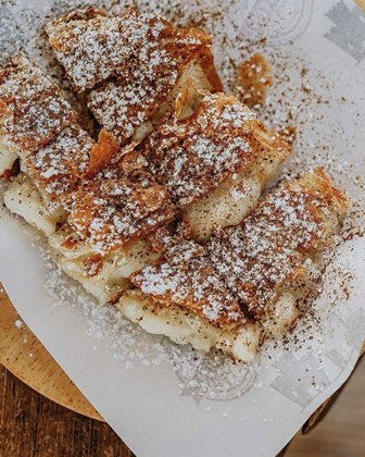 Stack of French toast slices dusted with powdered sugar on a white plate, resting on a wooden table.