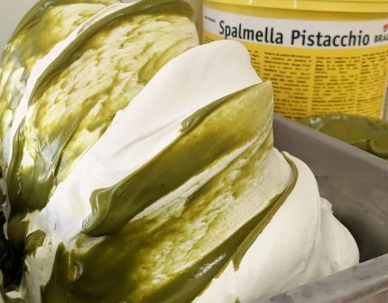 Close-up of green pistachio cream swirls on a tray, with a jar labeled 'Spalmella Pistacchio' in the background.