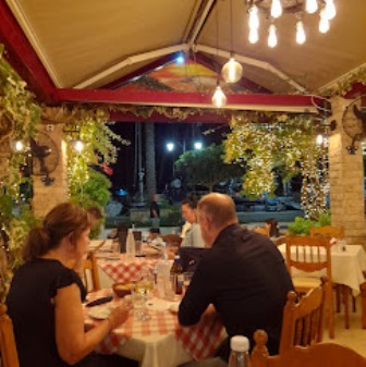 Outdoor restaurant patio at night with warm string lights, people dining at a table with a red-and-white checkered cloth.