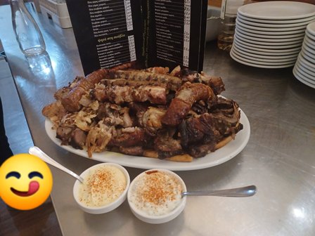 Plate of piled barbecue ribs with two small bowls of dipping sauce on a stainless-steel table, with menus and plates in the background.