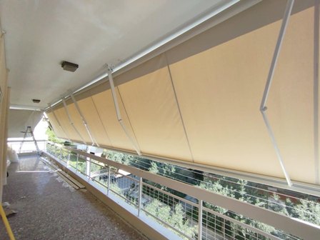 Exterior walkway with a large beige fabric shade sail suspended above, supported by metal poles and railing.