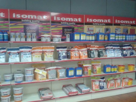 Store shelves lined with Isomat paint and building products; red Isomat signs top the display, with cans, buckets, and boxes neatly arranged on three shelves.