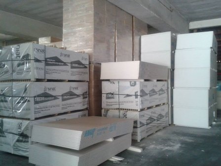 Warehouse interior with stacked insulation boards and packaged materials on a concrete floor.