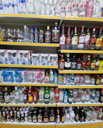 Store shelf filled with a variety of liquor bottles arranged on yellow shelves in a supermarket aisle.