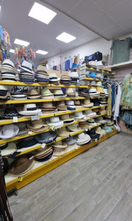 A hat shop aisle with many straw and sun hats stacked on yellow shelves along both sides, and clothes displayed on the right.