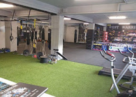 Indoor gym training area with turf, weights, and boxing bags for circuit workouts and cardio prep.