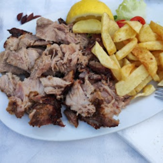 Plate of sliced roasted pork with French fries, a lemon wedge, and lettuce garnish.