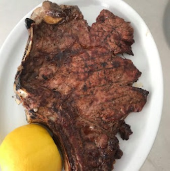 Grilled beef steak on a white plate with a lemon wedge on the side