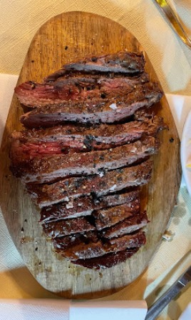 Sliced medium-rare steak on a wooden cutting board with salt grains nearby on a white napkin.