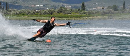 Man wakeboarding on a lake, wearing a life vest, as water sprays from his turn with the tow rope trailing behind.