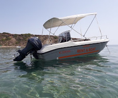 Small motorboat with an outboard engine, labeled 'RENT A BOAT', floating on clear water near a rocky shore with a canopy above.