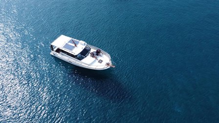 Aerial view of a white motorboat cruising on deep blue water, seen from above.