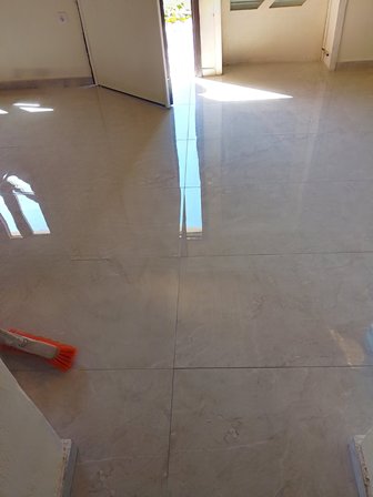 Shiny light-gray tiled floor in a doorway area, with an orange cleaning brush on the left.