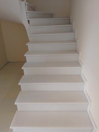 White indoor staircase with broad treads ascending to an upper floor, beige walls on both sides.