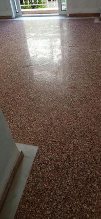 Shiny speckled terrazzo floor in a room with an open door at the far end showing a railing outside.