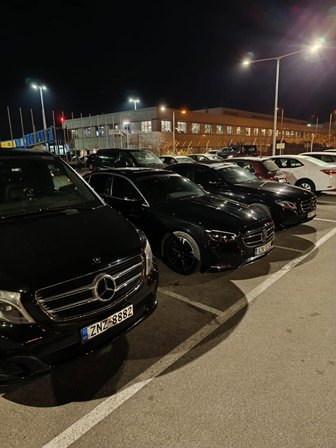 Row of black Mercedes-Benz cars parked in a well-lit lot at night, with a building and streetlights in the background.