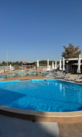 Outdoor pool area with bright blue water, white sun loungers, and closed white umbrellas under a clear blue sky at a resort.