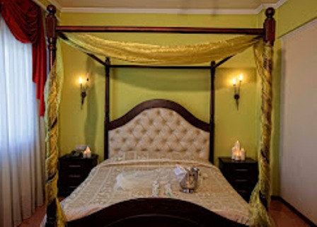 Luxurious four-poster bed with tufted headboard and gold canopy in a green bedroom, with matching linens and nightstands.