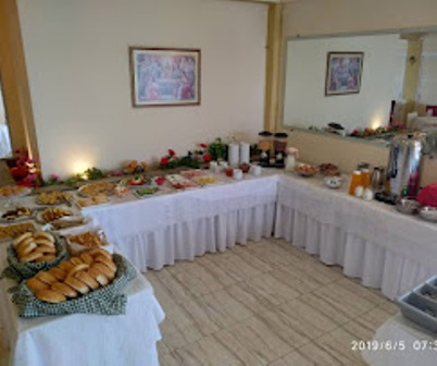 Buffet table set in a dining room with white cloths, bread rolls left, and assorted dishes along the long table; framed pictures on the walls.