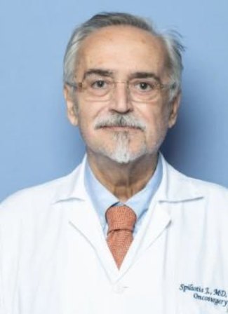 Senior male doctor with glasses, white coat, and orange tie, standing against a blue background.