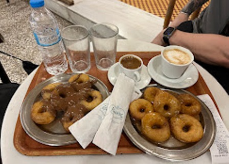 Outdoor cafe tray with two plates of donuts, a water bottle, two glasses, and two cups of coffee on a wooden table.