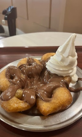Plate with a flower-shaped fried pastry topped with melted chocolate sauce and a swirl of vanilla soft-serve ice cream on the side.