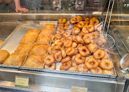 Bakery display case showing glazed donuts and rectangular frosted pastries on metal trays behind glass.