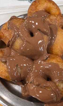 Pile of fried dough bites on a metal plate, generously smeared with chocolate spread or Nutella-like topping.
